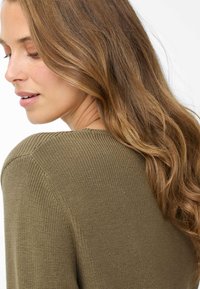 Olivgrüner Strickpullover mit strukturiertem Muster und rundem Ausschnitt. Leicht lockere Passform mit Nahtdetails und weichem Stoff.