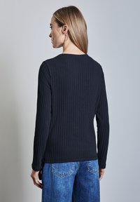 Top lungo a maniche nere a coste con scollatura rotonda, abbinato a jeans in denim azzurro chiaro con un classico design a cinque tasche.