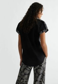 Top nero con maniche corte e dettagli decorativi sui polsi, abbinato a pantaloni larghi con stampa paisley in bianco e nero.