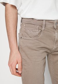 Beiga jeans i denim med smal passform, med en klassisk femficksdesign och subtila sömdetaljer på bakfickorna.