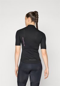 Svart kortermet sykkeltrøye med en tettsittende design, teksturert stoff, og rosa logo detalj på ryggen. Kombinert med svarte polstrede shorts.
