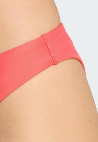 Koronkowe bikini dolne w kolorze koralowym, wykonane z gładkiego, elastycznego materiału, z wąskim pasem, bezszwowym wykończeniem i eleganckim designem.