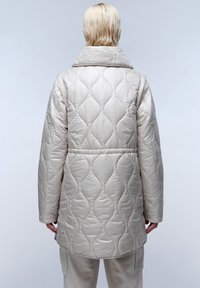 Béžová prošívaná péřová bunda s vysokým límcem, nadměrným střihem a hladkou texturou, s vzorovaným designem na látce.