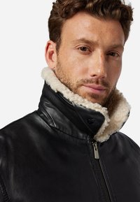 Zwarte leren jas met een hoge, fleece-gevoerde kraag en ritssluiting aan de voorkant. Glad textuur met een minimalistisch ontwerp.