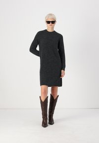 Σκούρο γκρι πλεκτό φόρεμα με μακριά μανίκια, στρογγυλή λαιμόκοψη, συνδυασμένο με καφέ δερμάτινες μπότες καουμπόικου στιλ που έχουν διακοσμητικά ραψίματα.