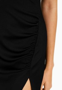 Svart klänning med ribbad textur, sidofåll och hög slitsdesign som framhäver en figurnära form och mjuk drape.