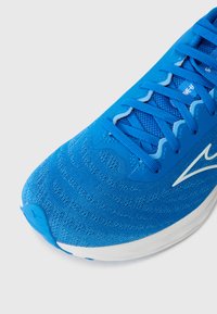 Zapatilla deportiva azul con un upper de malla texturizada, cordones en contraste y una mediasuela blanca. Presenta una puntera redondeada y un detalle de marca sutil.