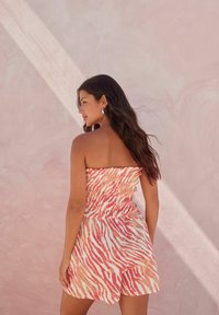 Mono sin tirantes con cintura fruncida en un patrón de rayas de cebra en rosa y naranja, hecho de tela ligera, con un ajuste relajado.