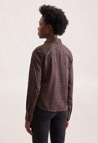 Camicia button-up in tessuto scuro con un motivo geometrico in tonalità di marrone e nero, dotata di colletto e maniche lunghe.