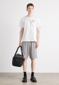 White cotton t-shirt with red graphic, gray linen shorts, black leather duffle bag, and black shoes with double buckle. Smooth textures.