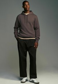 Lilla tekstureret hoodie med snoretræk, lagd oven på en cremefarvet skjorte, parret med sorte vide bukser og hvide sneakers med grønne striber.