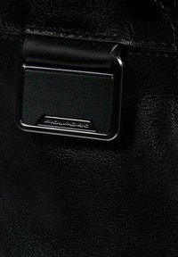 Detalle de un bolso de cuero negro con un cierre metálico que presenta un logo grabado y una superficie texturizada, resaltando un diseño elegante y durabilidad.