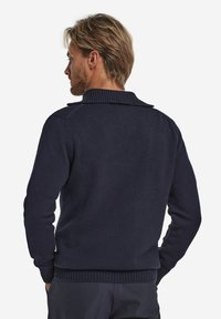 Dunkelblauer Strickpullover mit geripptem Kragen und Bündchen, langen Ärmeln und einer taillierten Form ohne sichtbare Verschlüsse.