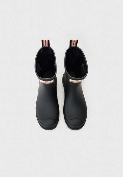 Bottes noires en caoutchouc jusqu'aux chevilles avec une finition lisse, dotées d'une languette orange et blanche et d'un doublure intérieure noire à motifs.
