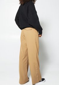 Svart ribbad stickad tröja tillsammans med beige vida byxor med framveck och fickor, mot en neutral bakgrund.