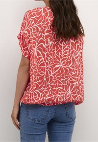 Blusa de patrón floral rojo y blanco con un corte holgado, mangas cortas y una tela texturizada. Combinada con jeans de mezclilla azules.