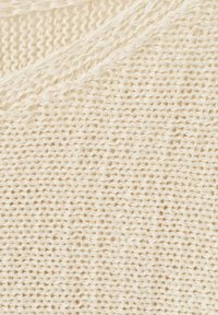 Gros plan d'un tissu tricoté de couleur crème montrant des mailles bouclées détaillées et un motif en torsades.