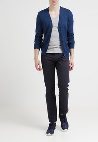 Marinblå kofta med knappar, ljusgrå t-shirt under, mörka byxor och marinblå sneakers. Slät textur och enkel design.