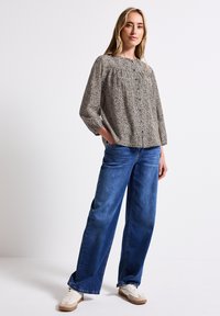 Lätt, mönstrad blus med knappstängning och rynkad halsringning, i kombination med lösa blå denimbyxor och vita sneakers.