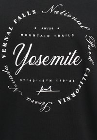 T-shirt in cotone nero con testo stampato bianco in vari caratteri. Elementi notevoli includono "Yosemite," "Vernal Falls," e le coordinate sottostanti.