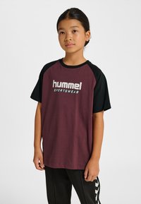 Vinröd och svart raglan-t-shirt med rund halsringning, med vit "hummel"-logotyp och texten "SPORTSWEAR". Mjuk bomullstyg, avslappnad passform.