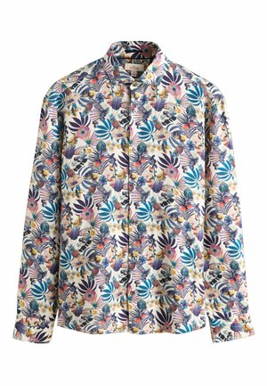 Szakállas férfi, aki gombolt trópusi ingben van, színes virág- és gyümölcsmintákkal, a gallérra és a felső mellkasra fókuszálva.