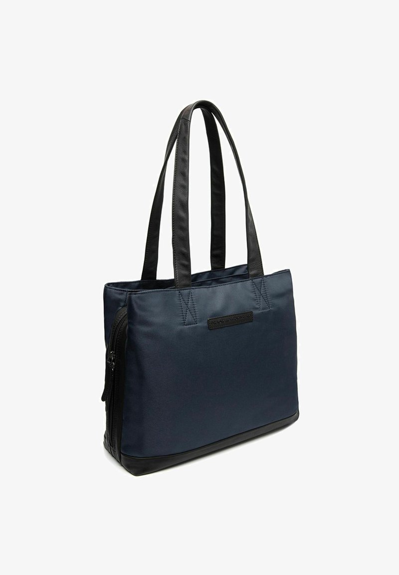 Bolsa tote de tela azul marino con acentos de cuero sintético negro, bolsillo lateral con cremallera y asas suaves dobles para un fácil transporte.