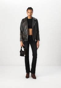 Giacca da moto in pelle nera con accessori in metallo argentato, abbinata a un top corto nero e jeans neri a vita alta. Stivali marroni con tacco e una borsa piccola.