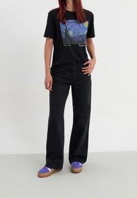 Camiseta negra con un gráfico de "Noche Estrellada", combinada con jeans negros de cintura alta. Lleva zapatillas moradas para un contraste.