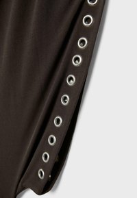 Zbliżenie na ciemną tkaninę z pionowym rzędem metalowych oczek wzdłuż krawędzi, ukazujące fakturę i detale.