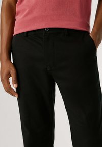 Zwarte katoenen broek met een slanke pasvorm, voorzien van een knoopsluiting, steekzakken aan de voorkant en een gladde textuur. Draagt een roze top.