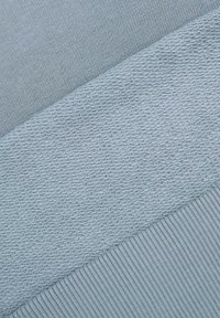 Jasnoniebieska włóczka o gładkiej fakturze, z dwoma kontrastującymi wzorami: drobnym splotem i teksturowanym, prążkowanym wzorem.