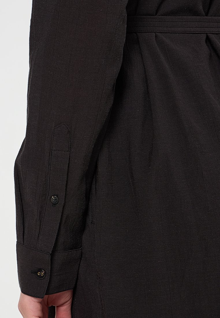 Schwarzes Langarmshirt mit Leinenstruktur, ausgestattet mit einem Ein-Knopf-Manschette und passendem Stoffgürtel, das ein sauberes, minimalistisches Design präsentiert.