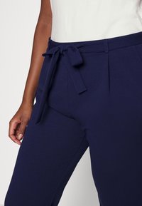 Navy blue trousers with a smooth texture, featuring a tied waistbelt and pleated front. The fabric appears lightweight and structured.
