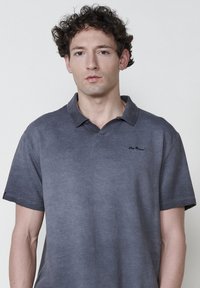 Polo shirt gris à manches courtes en tissu texturé. Doté d'un col et d'un logo discret sur la poitrine gauche. Design simple avec une allure légère.