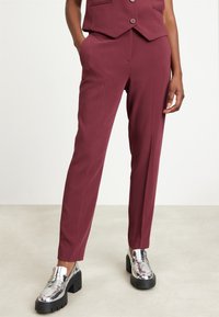 Vinröda skräddarsydda byxor med rak ben och fickor, i kombination med blanka silverfärgade loafers med en kraftig svart sula.