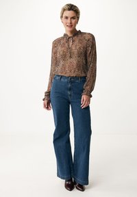 Brun mønstrede bluse med en nøglehulsudskæring og flæseærmer, parret med mørkeblå bootcut jeans og maroon hæle.