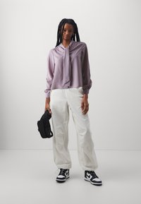 Light purple blouse with a tie detail, paired with white baggy pants. Black crossbody bag and black-and-white sneakers complete the look.