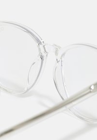 Lunettes en plastique transparent avec des verres ronds, présentant une texture lisse et des accents argentés minimaux sur les branches.