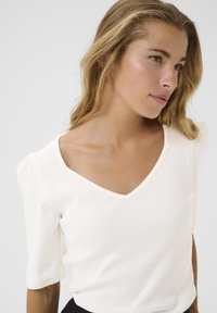 Maglietta bianca a maniche corte con scollatura a V profonda. Presenta un design aderente e una consistenza morbida, con un leggero volume sulle maniche.