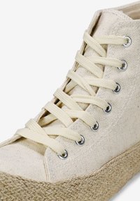 Zapatilla alta de lona beige con cordones beige, ojales plateados y suela de plataforma de yute natural. Tejido texturizado y diseño sencillo.