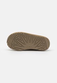 Suola in gomma marrone con un motivo zigzag testurizzato e logo UGG; tacco piatto e arrotondato per una migliore trazione e stabilità.