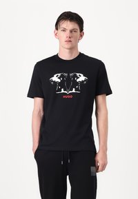 Black cotton T-shirt featuring a graphic print of two dog heads in white, with "HUGO" in red text beneath the design. Short sleeves.