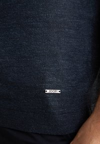 Ciemnoniebieski sweter z dzianiny o subtelnej teksturze i metalową metką z napisem "JOOP!" na dolnym końcu. Casualowy design, dopasowany krój.