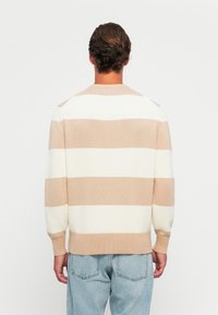 Beige och vitrandig tröja med rund hals, stickad struktur och ribbad mudd och nederkant. Bärs med ljusblå jeans.