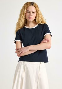Marineblauwe t-shirt van zacht materiaal, met witte biezen op de halslijn en mouwen. Rechstreeks model, korte mouwen en een losse pasvorm.