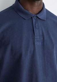 Marinblå polo skjorta i bomull. Har krage, två knappar och diskret broderad "BOSS" logotyp på bröstet.