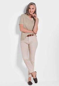 Beige kortemouw V-hals top, lichtbeige aansluitende broek, bruine riem en zwarte gestructureerde instappers, met een neutrale achtergrond.