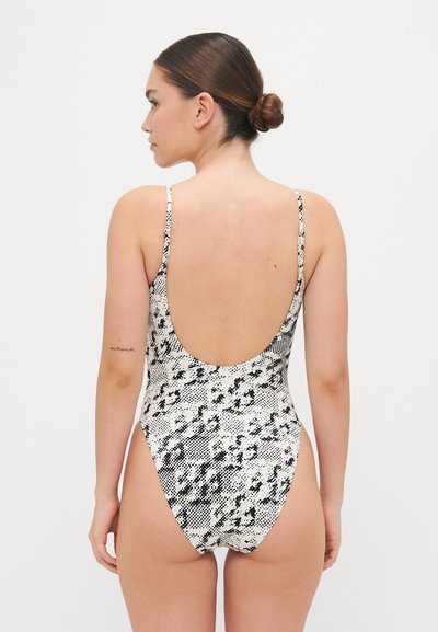 Maillot de bain imprimé serpent en noir et blanc avec des bretelles étroites et un dos bas ; design ajusté, texture lisse, jambes de coupe moyenne et sans matériel visible.