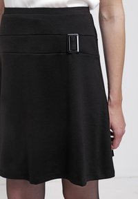 Mustat hameet, joissa on sovitettu vyötärö ja litteä solkidetali. Valmistettu sileästä kankaasta, se omaa A-linjaisen leikkauksen ja hienovaraisen tekstuurin.